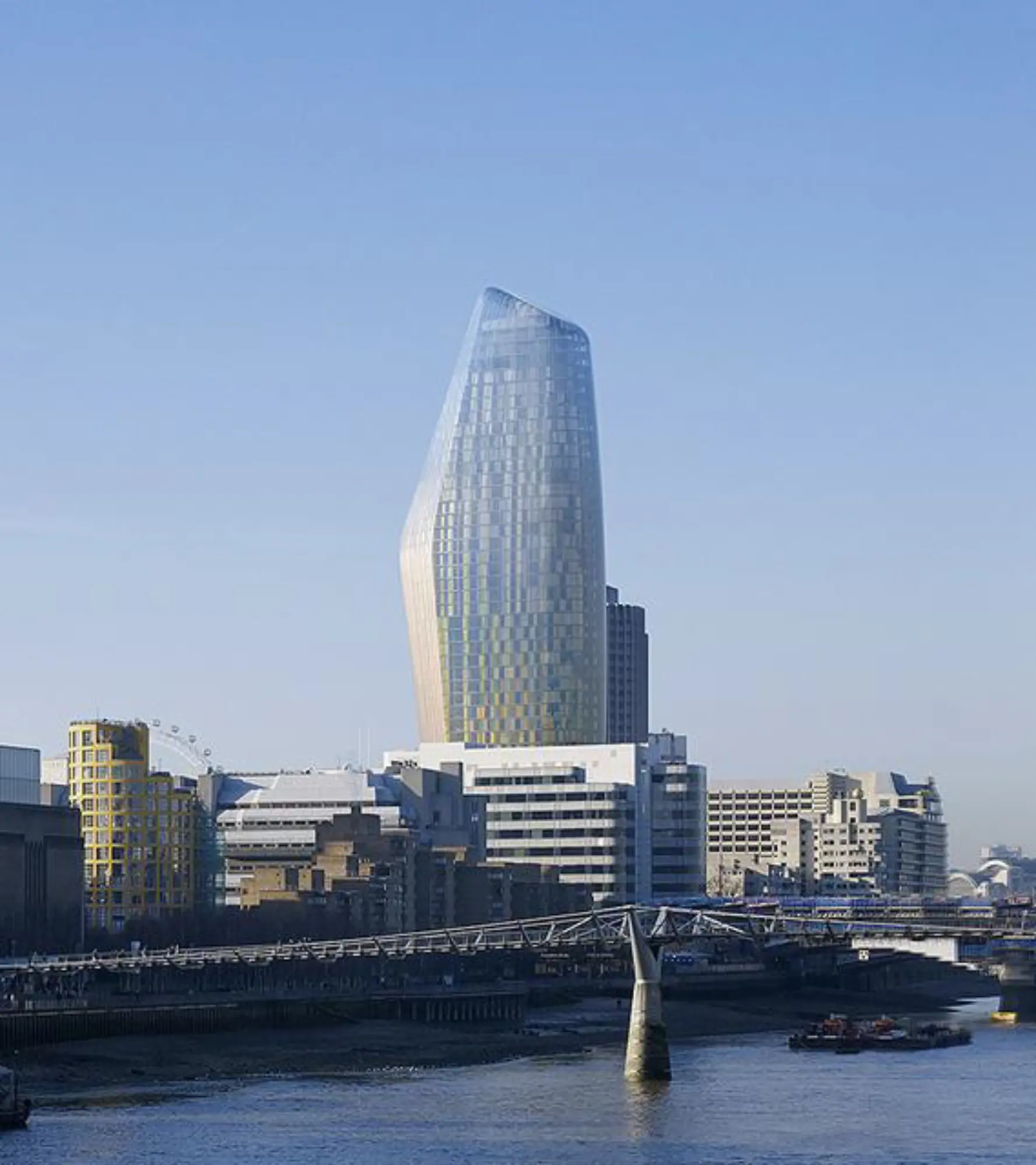 Modern skyscraper beside river and bridge.