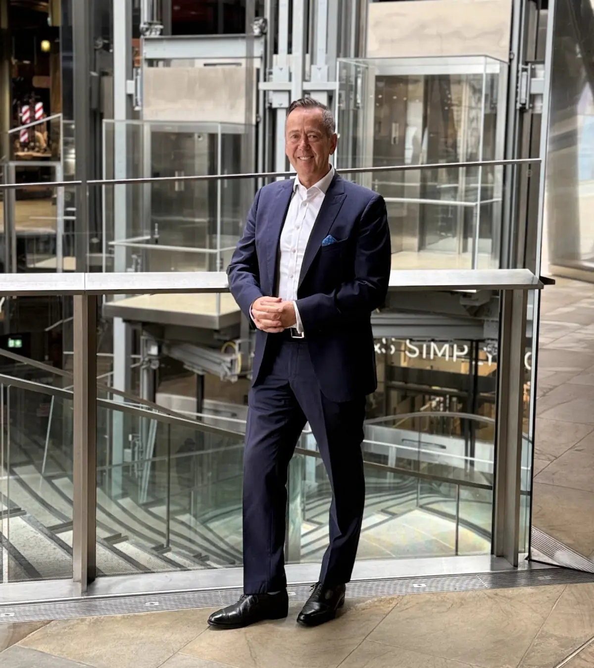 Man in suit standing by glass railing.