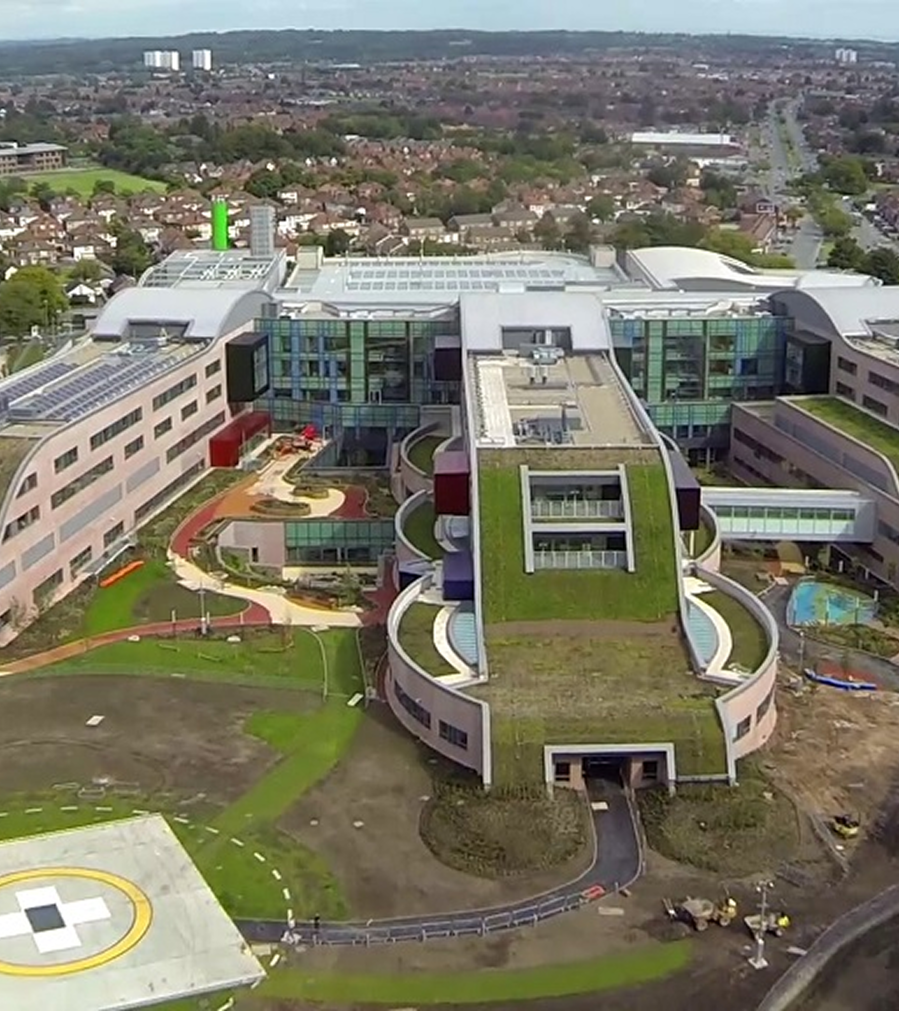 A modern hospital complex with green roofs and surrounding greenery.