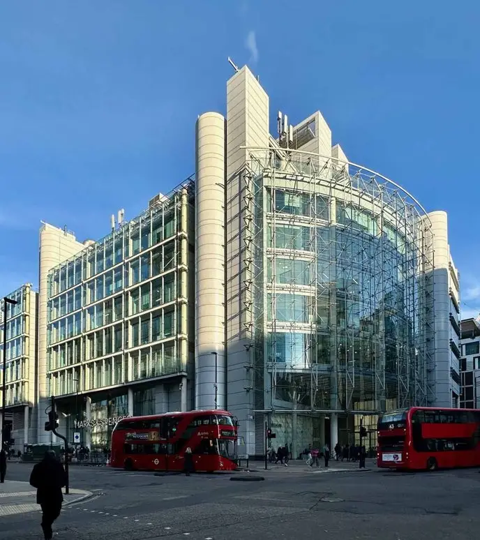 Modern glass office building with red double-decker buses in front.