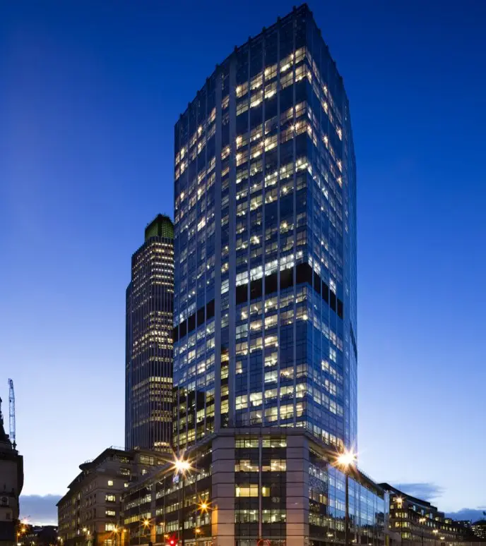 Modern glass skyscraper illuminated at dusk in a cityscape.